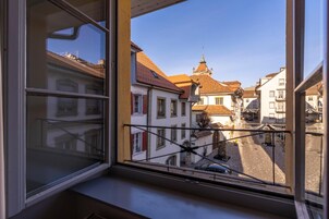 Vista desde una ventana que da a una calle con edificios tradicionales, una aguja de iglesia y un cielo despejado.
