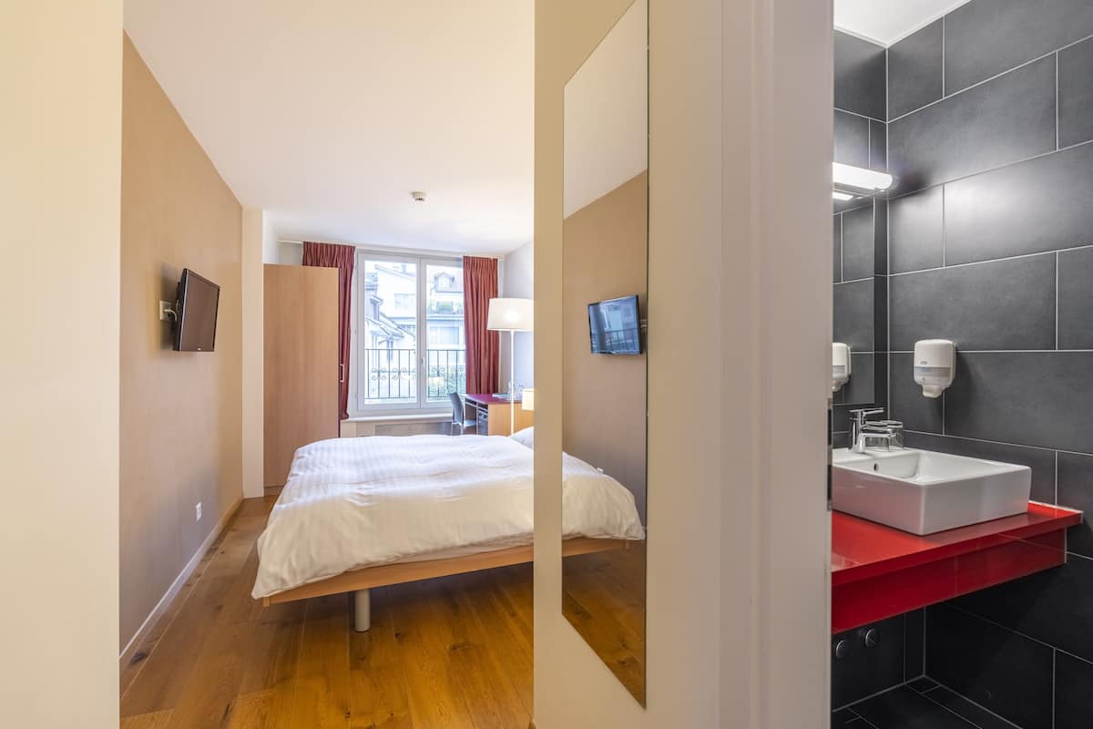 Quarto de hotel com cama, televisão, banheiro com pia e vista para o exterior.