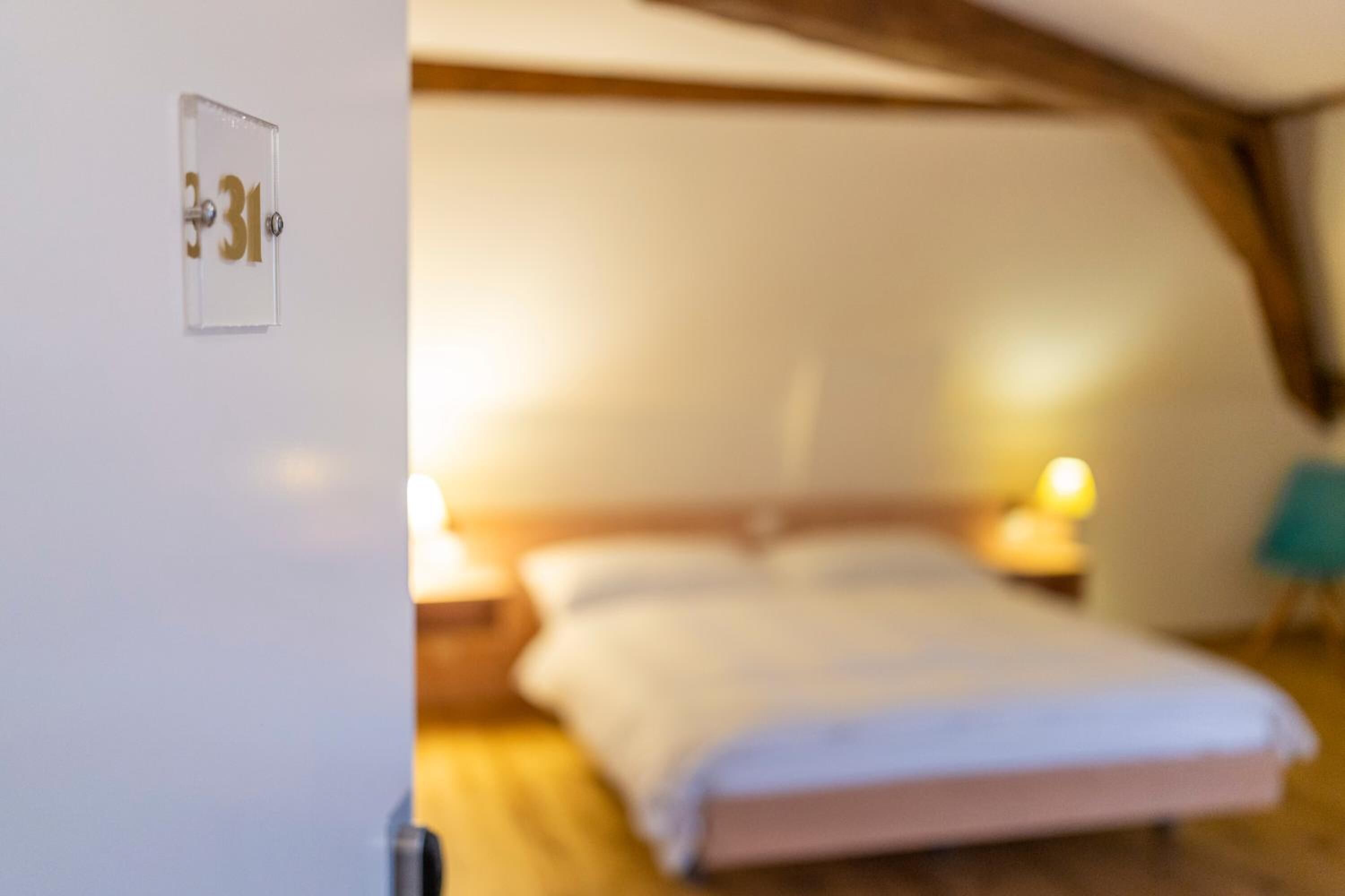 A bedroom with a bed, bedside lamps, and a door with a number plate.