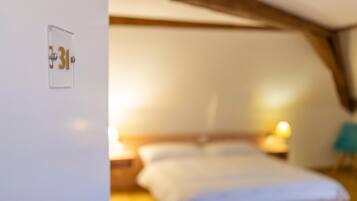 A bedroom with a bed, bedside lamps, and a door with a number plate.