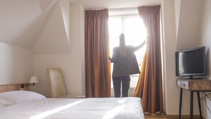 Una habitación de hotel con una cama, una silla, un televisor y cortinas.
