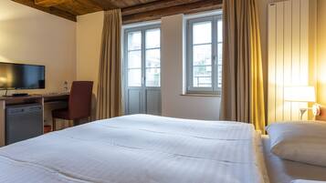 A hotel room with a bed, a desk with a chair, a television, and a window with curtains.
