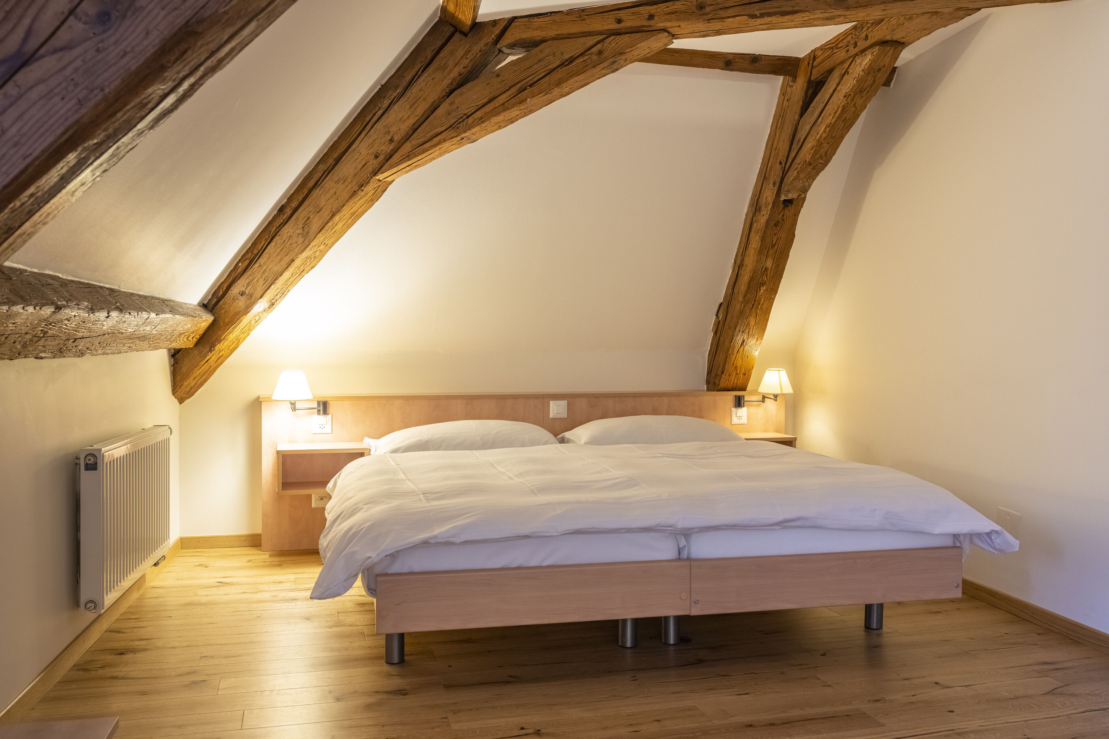Un dormitorio con techo de madera, una cama con ropa de cama blanca, dos lámparas de noche y una mesita de noche de madera.
