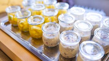 Un plateau contenant divers aliments, notamment des bocaux avec des contenus jaunes et bruns, qui pourraient être des cornichons ou des confitures, le tout posé sur un plateau en métal.