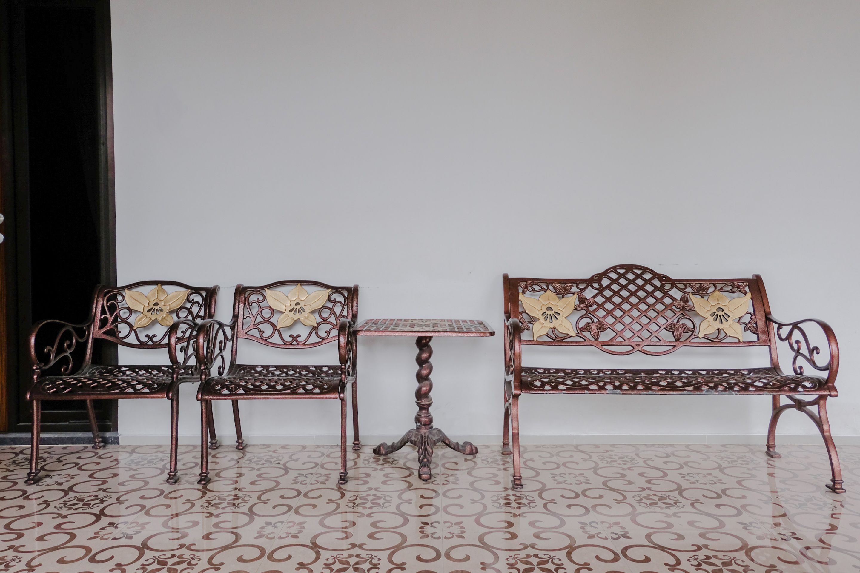 A room with a patterned floor, a wooden bench with floral designs, and a small table with a square top.