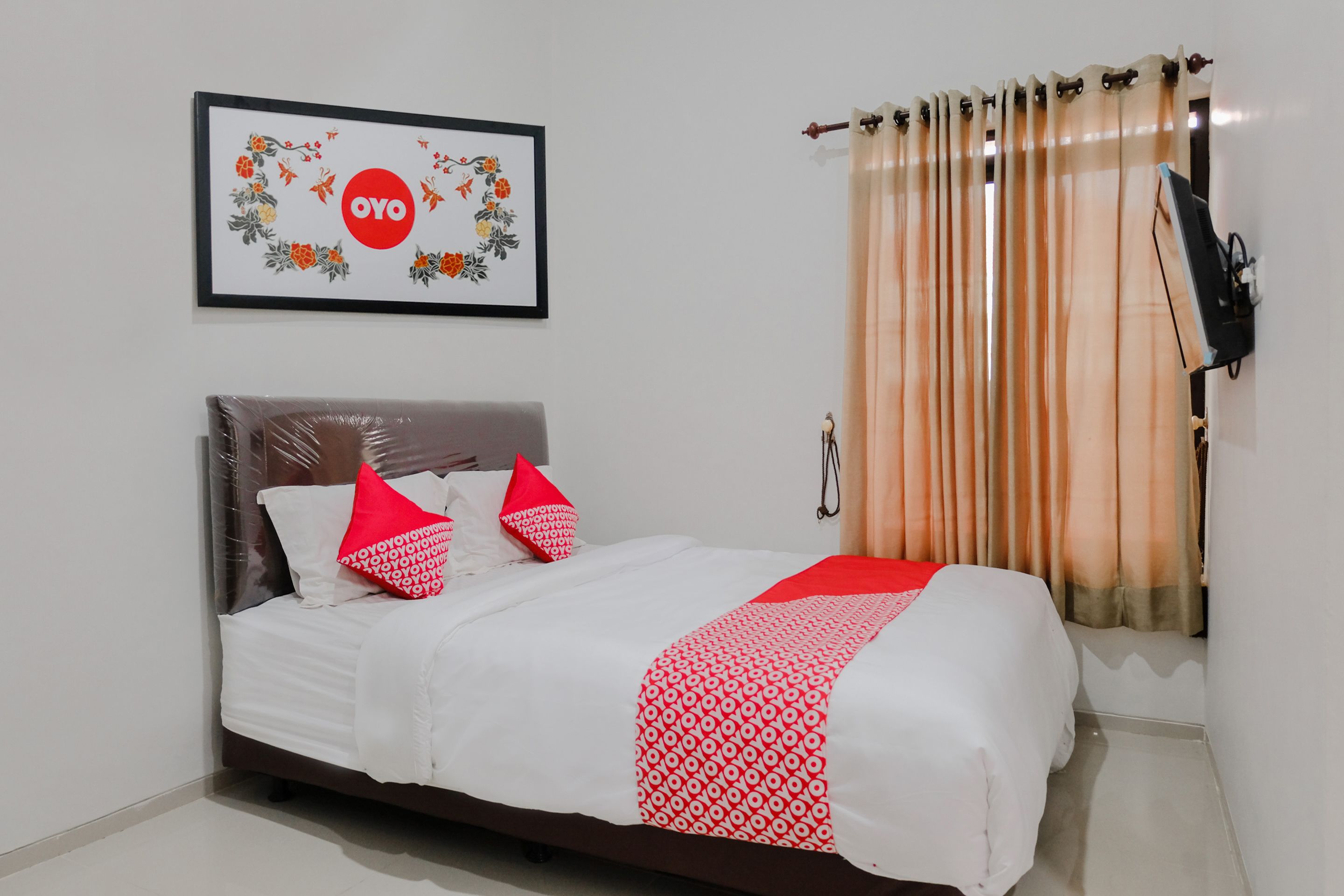 A bedroom with a bed, pillows, a blanket, a wall-mounted TV, and a window with curtains.