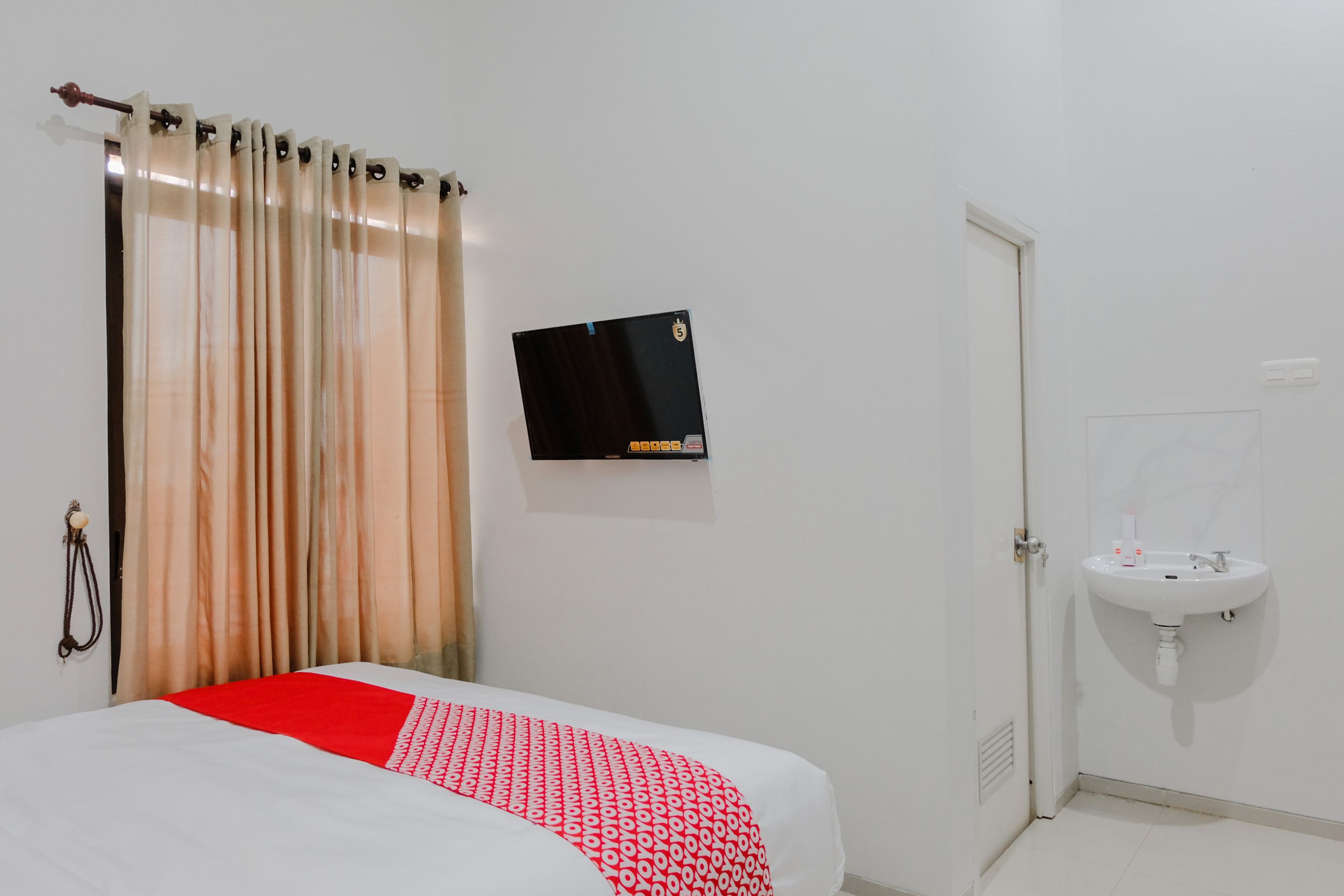 Una habitación de hotel con cama, televisor montado en la pared, lavamanos y puerta.