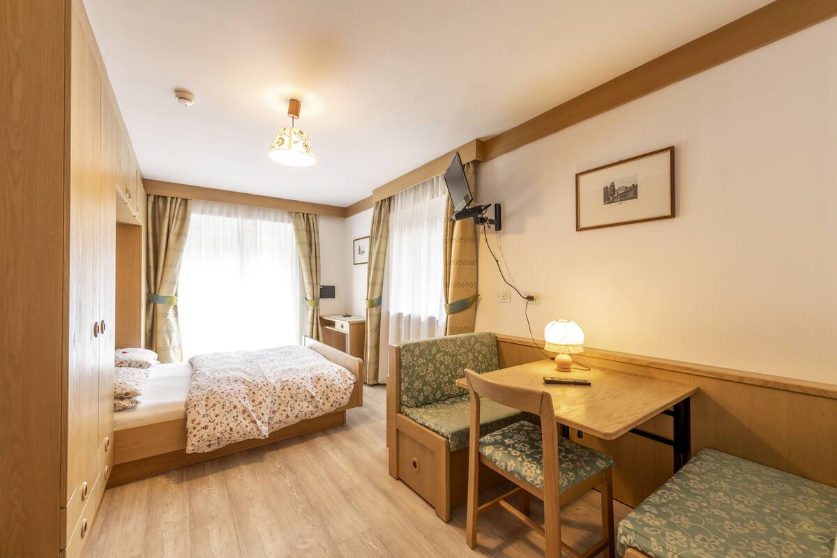 Habitación compacta con cama, escritorio y silla. Una lámpara está sobre el escritorio, un cuadro en la pared y una ventana con cortinas.
