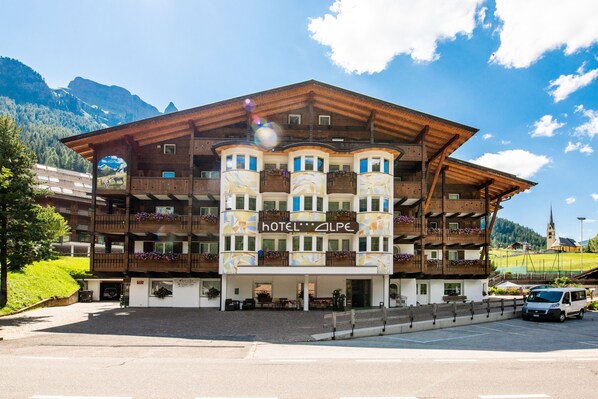 A multi-story hotel with balconies, a sign reading "HOTEL ALPE", and a mountainous backdrop. - Hotel Alpe (Canazei)