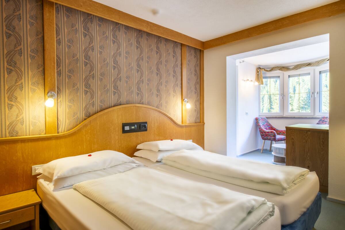 Habitación de hotel con dos camas, cabecera de madera, un escritorio pequeño y una silla.