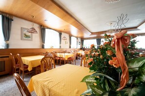 A restaurant with wooden interiors, yellow tablecloths, and a flower arrangement on the table. - Hotel Alpe (Canazei)