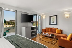 Una camera d'albergo moderna con un letto, una poltrona, un tavolino, una televisione e un balcone con vista.