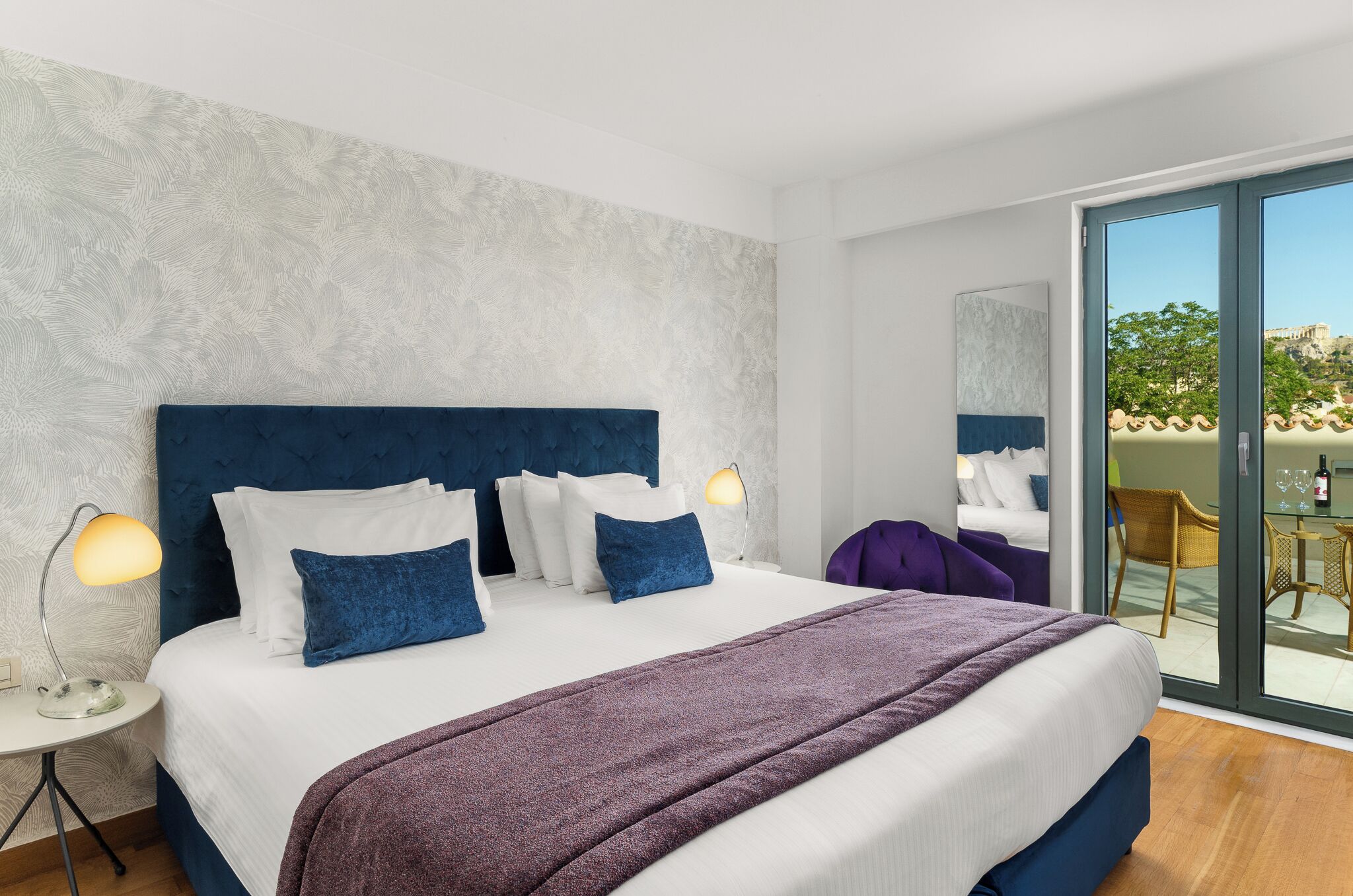 Moderni hotellihuone, jossa on suuri sänky, yöpöytä, lamppu ja näkymä lasiovesta.