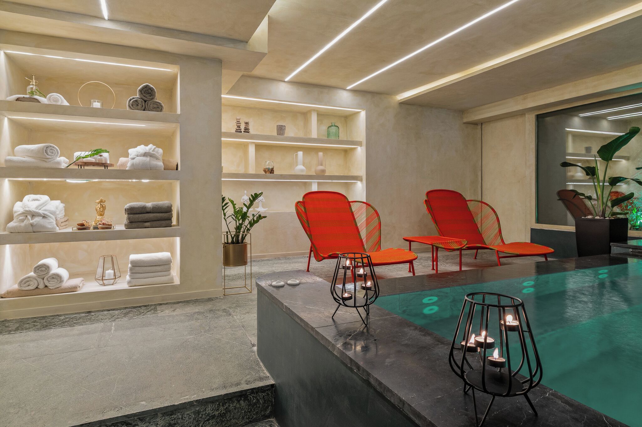 Uma área de spa com piscina, cadeiras vermelhas, prateleiras com toalhas e uma planta em vaso.