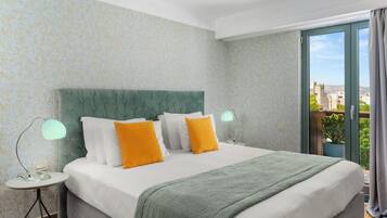 Habitación de hotel con cama, mesita de noche, lámpara y vista a la ciudad a través de un ventanal grande.