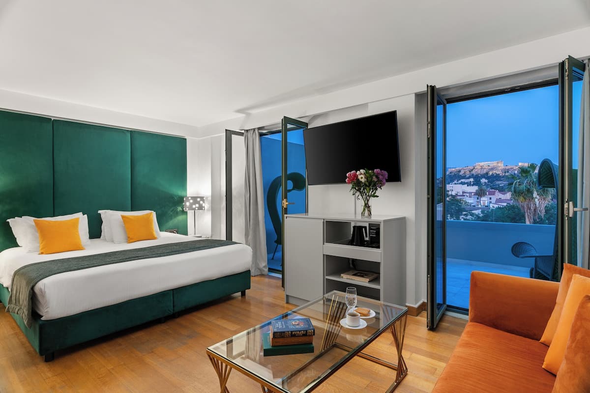 A modern hotel room with a large bed, a sofa, a TV, and a balcony with a city view.