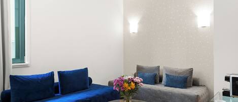 A modern room with a blue sofa, a grey sofa, and a glass coffee table with a vase of flowers.