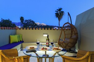 Un comedor con una mesa de vidrio, sillas de mimbre y vistas a un edificio histórico.