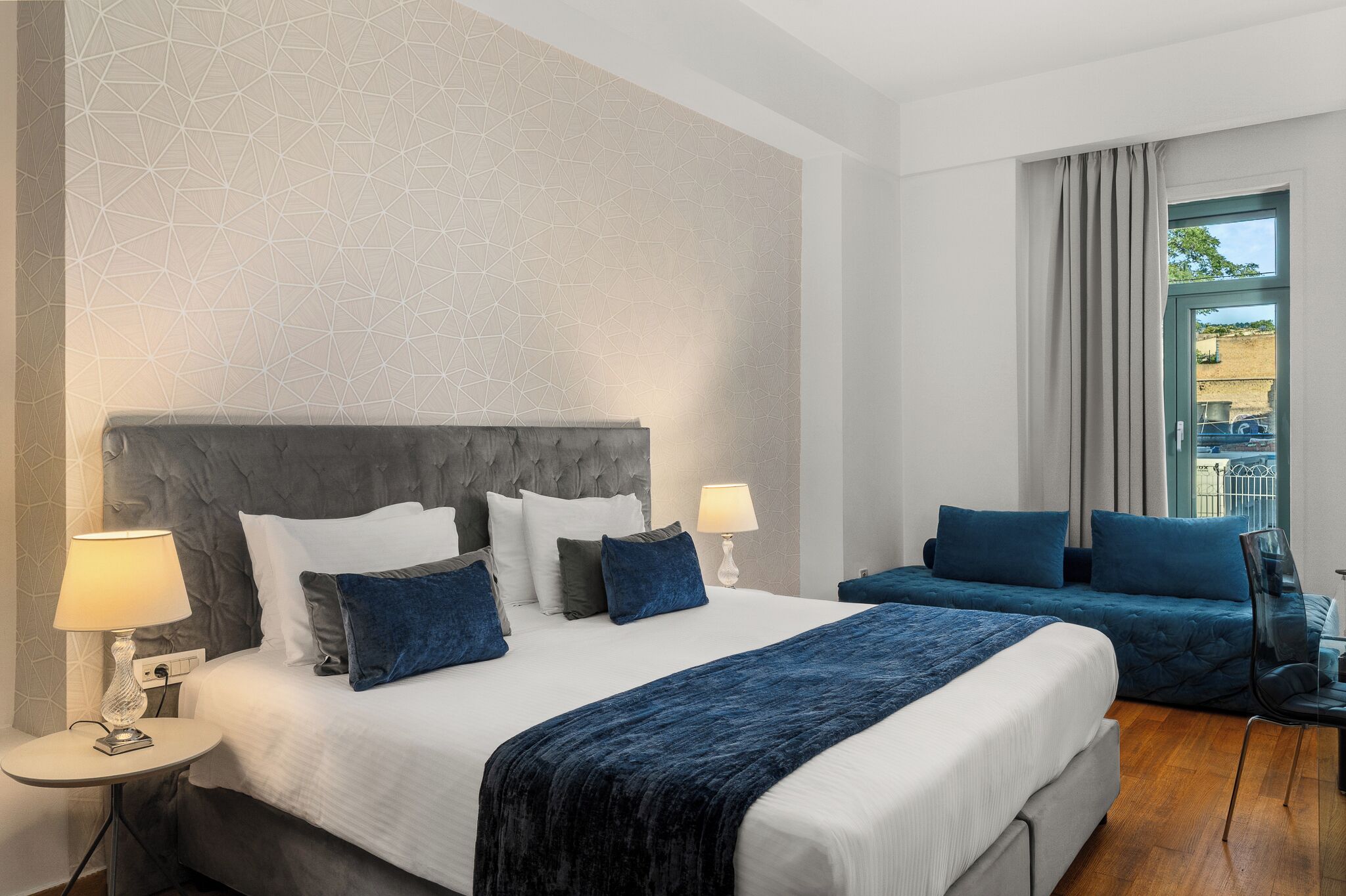 Une chambre d’hôtel moderne avec un grand lit, deux tables de chevet, un canapé et une vue sur l’extérieur.