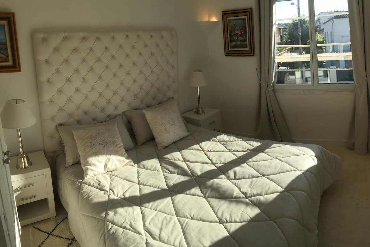 A neatly made bed with a tufted headboard, two bedside tables with lamps, and a window with curtains.