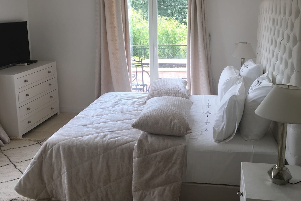 A bedroom with a bed, a dresser, a TV, and a window with curtains.