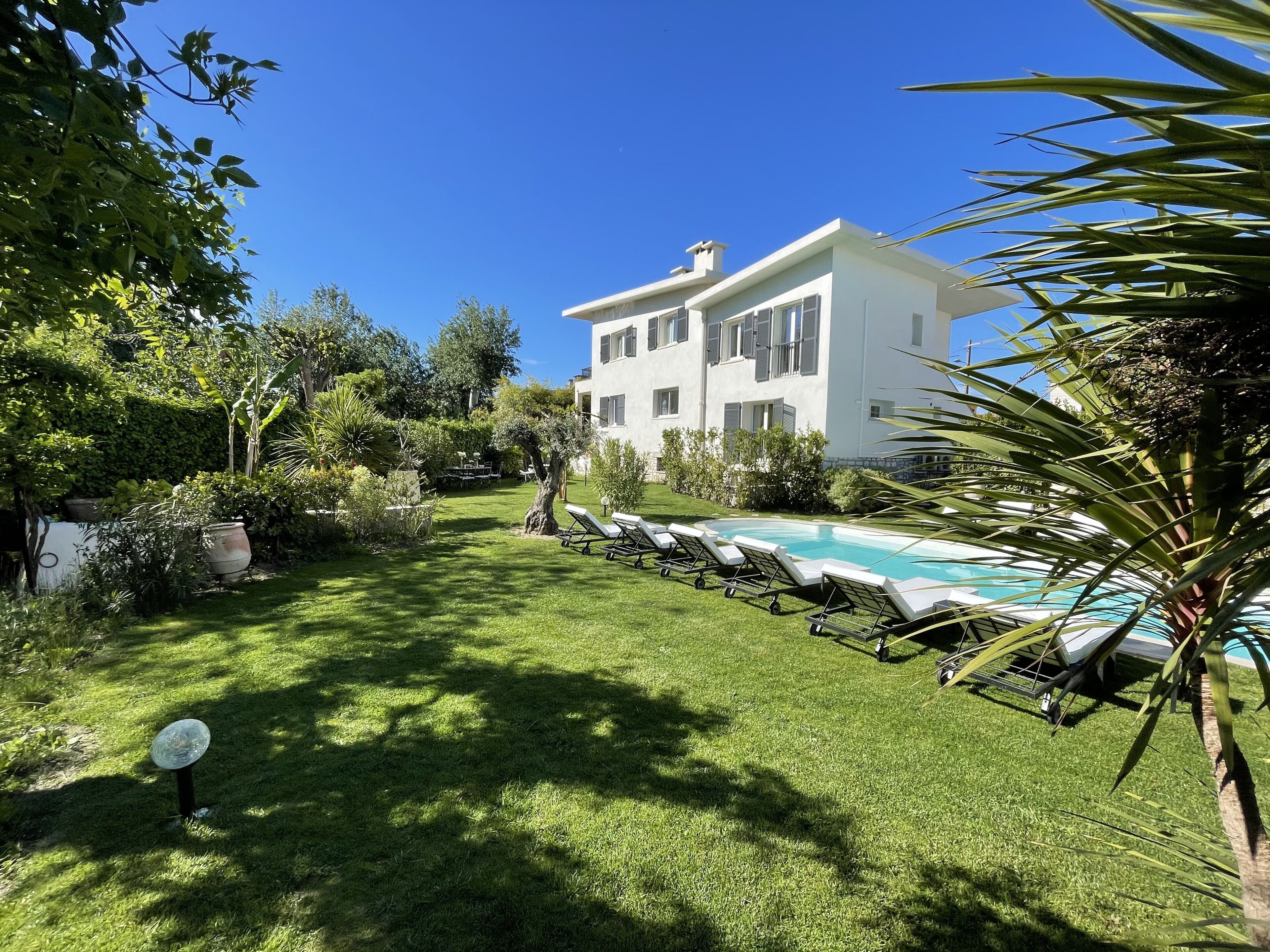 Una villa blanca con piscina, rodeada de exuberante vegetación y un césped cuidado.