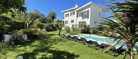 Una villa blanca con piscina, rodeada de exuberante vegetación y un césped cuidado.