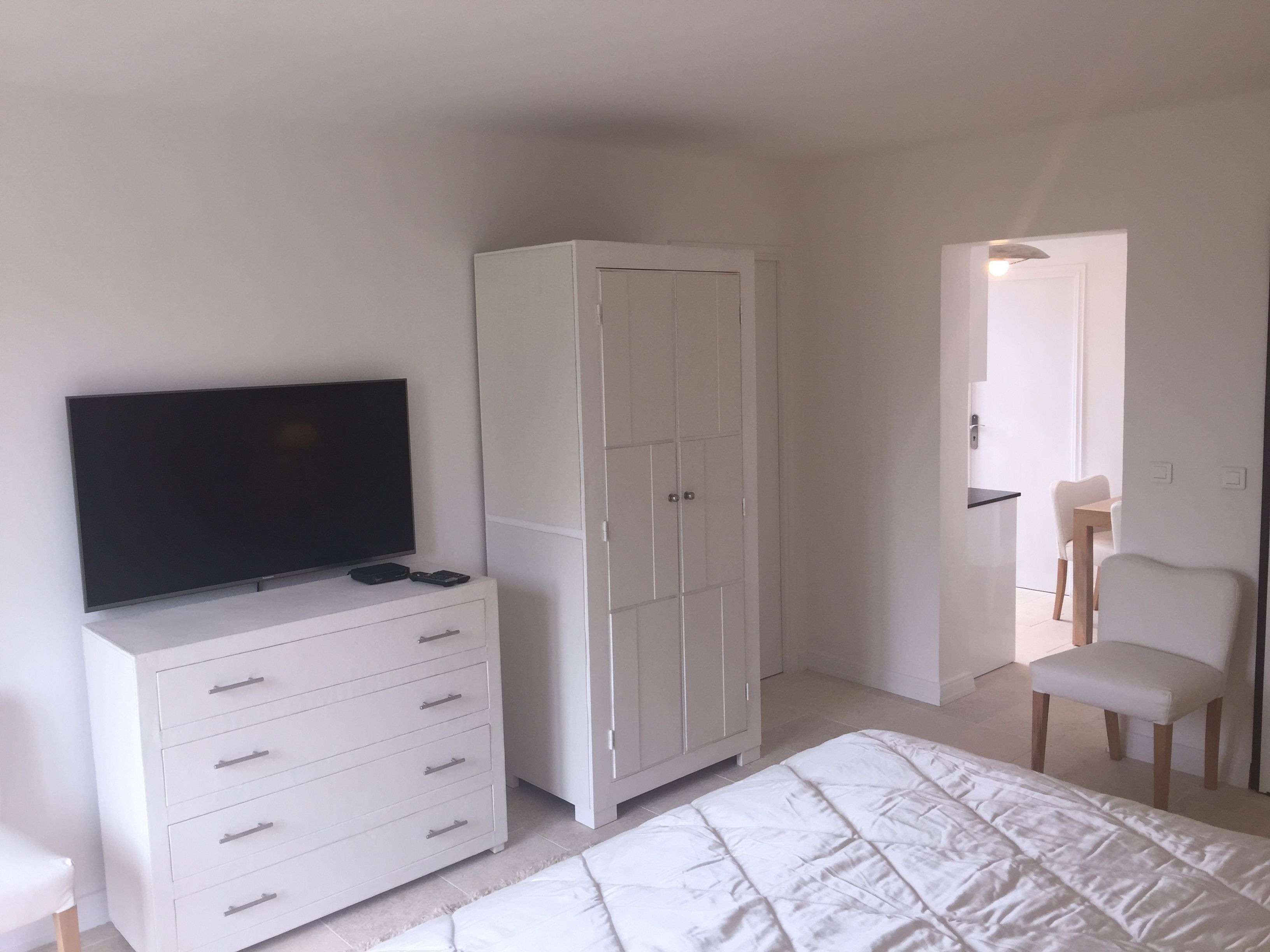 Ein Schlafzimmer mit einem Bett, einem Fernseher auf einer Kommode, einem Kleiderschrank und einem Sessel.