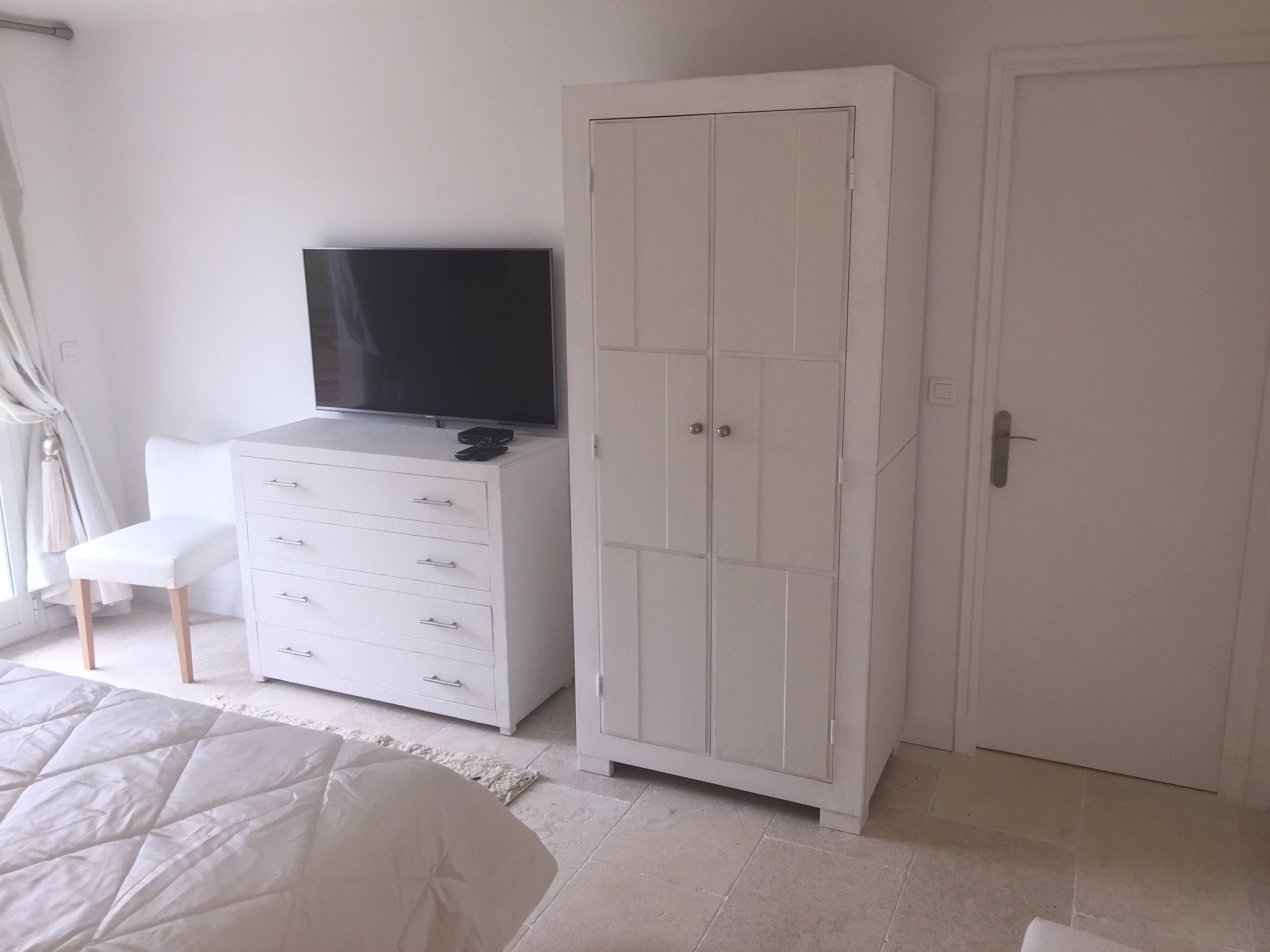 Una camera da letto con un letto, una cassettiera bianca con un televisore, un armadio e una porta.