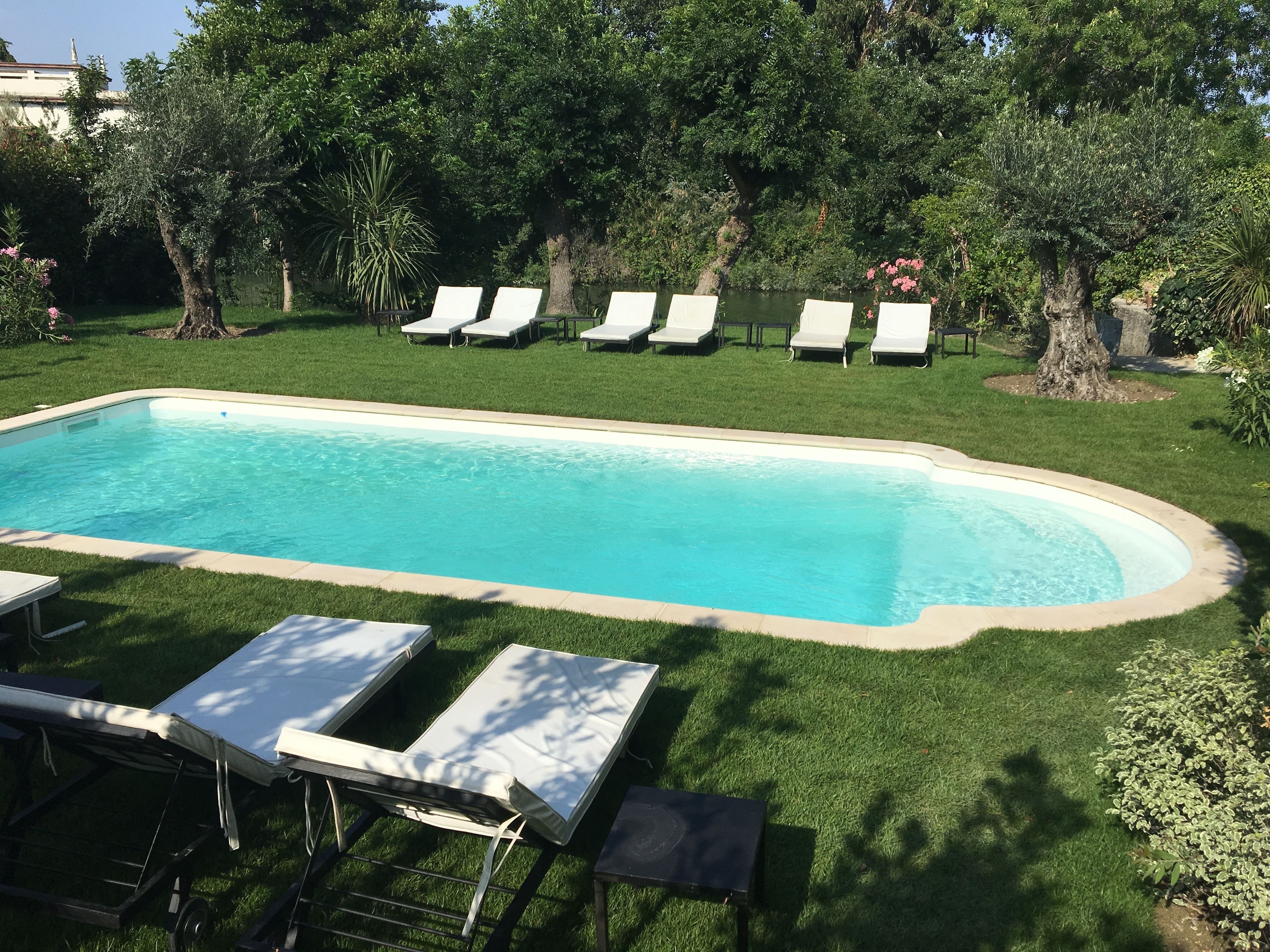 A rectangular swimming pool with a tiled edge, surrounded by a well-maintained lawn and several white lounge chairs.