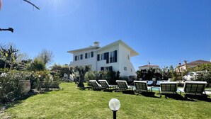 A two-story house with a white exterior and black shutters, surrounded by a well-maintained lawn and several lounge chairs. - Villa Louise-Rose (Villeneuve-Loubet)