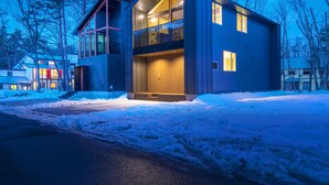 A modern two-story house with a balcony, large windows, and a snow-covered driveway. - Grey Wolf Chalet (Hakuba)