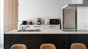 A modern kitchen with a central island, a built-in oven, and a microwave. - Grey Wolf Chalet (Hakuba)