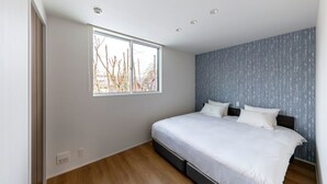 A bedroom with a large window, a bed with white bedding, and a blue textured wall. - Grey Wolf Chalet (Hakuba)