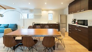 A modern kitchen with a wooden dining table, dark cabinets, and built-in appliances. - Black Crane Chalet (Hakuba)