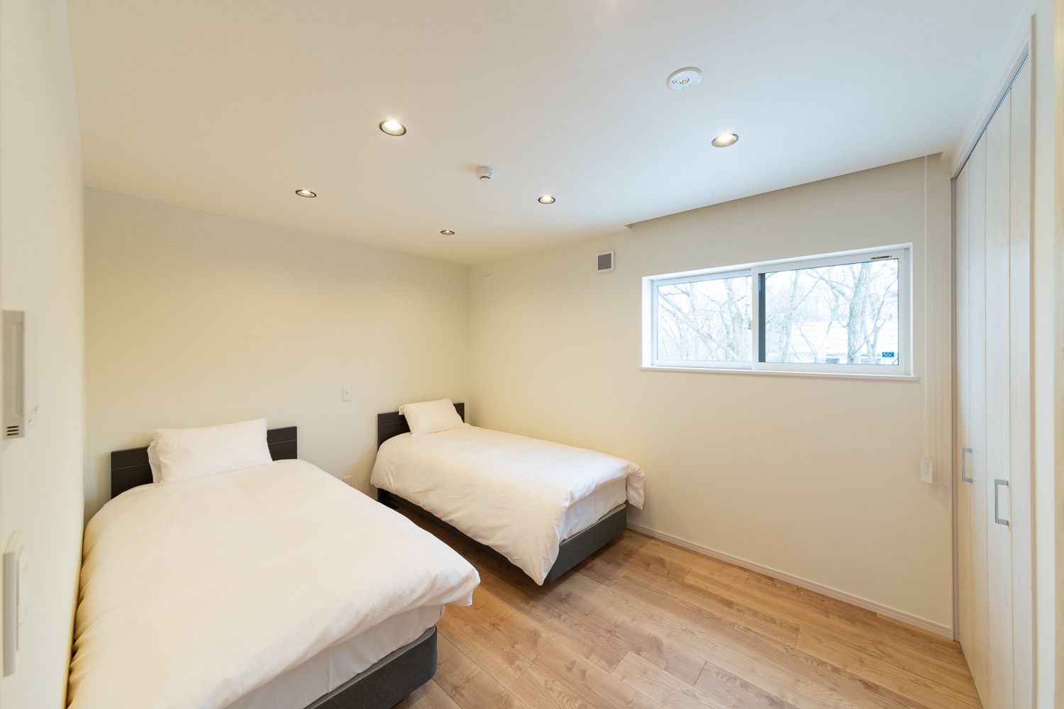 Een slaapkamer met twee bedden, een raam en inbouwspots.
