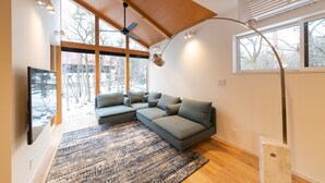 A modern living room with a sectional sofa, large windows, and a ceiling fan. - Black Crane Chalet (Hakuba)