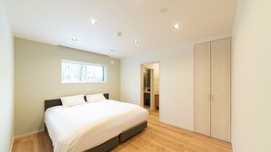 A modern bedroom with a large bed, wooden flooring, a wardrobe, and a shower area. - Black Crane Chalet (Hakuba)