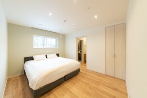 Quarto moderno com uma cama grande, piso de madeira, guarda-roupa e área de chuveiro.