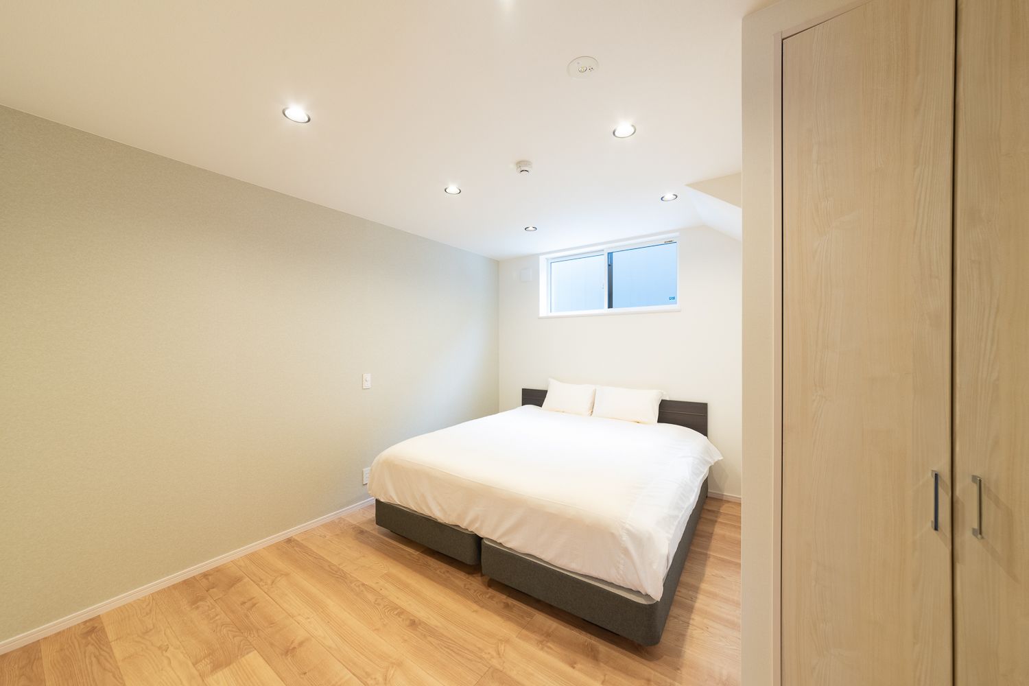 Een slaapkamer met een bed, houten vloeren, een raam en een kledingkast.
