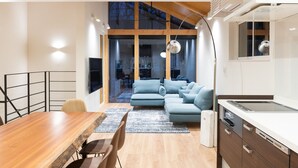 A modern kitchen with a built-in oven, a dining area with a wooden table and chairs, and a blue sofa in the living area. - Black Crane Chalet (Hakuba)