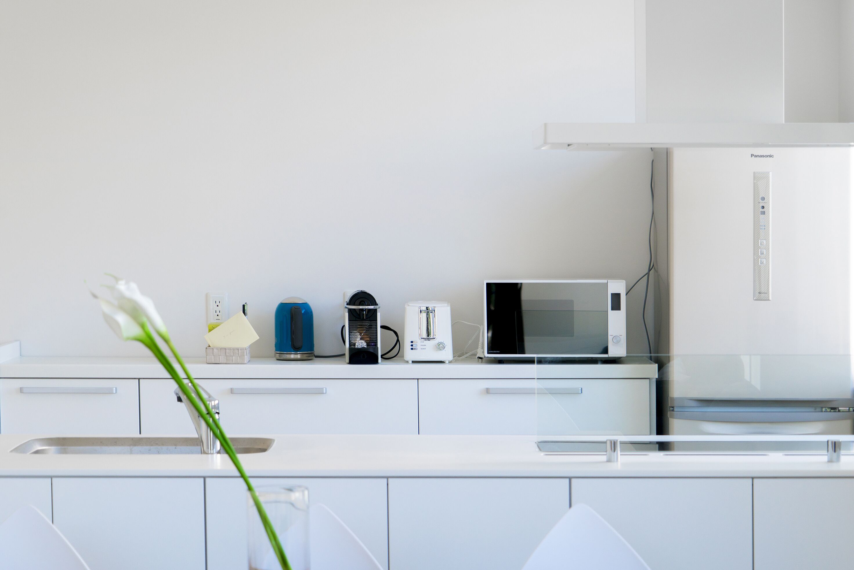 A modern kitchen with white cabinetry, a microwave, a coffee maker, and a kettle on the counter.