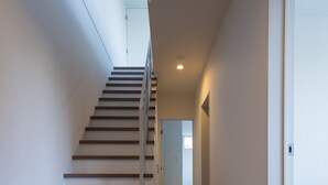 A modern interior with a wooden staircase leading to a landing, white walls, and a hallway with a door at the end. - White Fox Chalet (Hakuba)