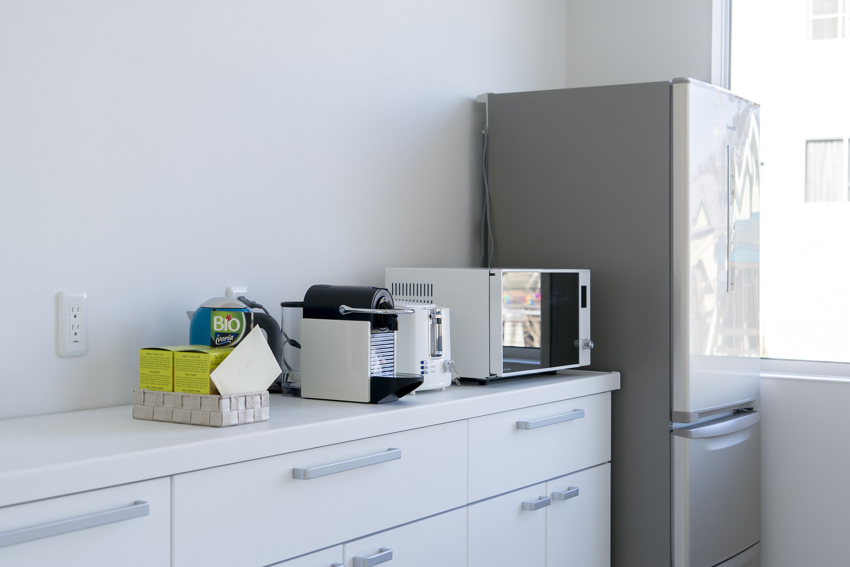 Una cocina con refrigerador, microondas y cafetera sobre la encimera.