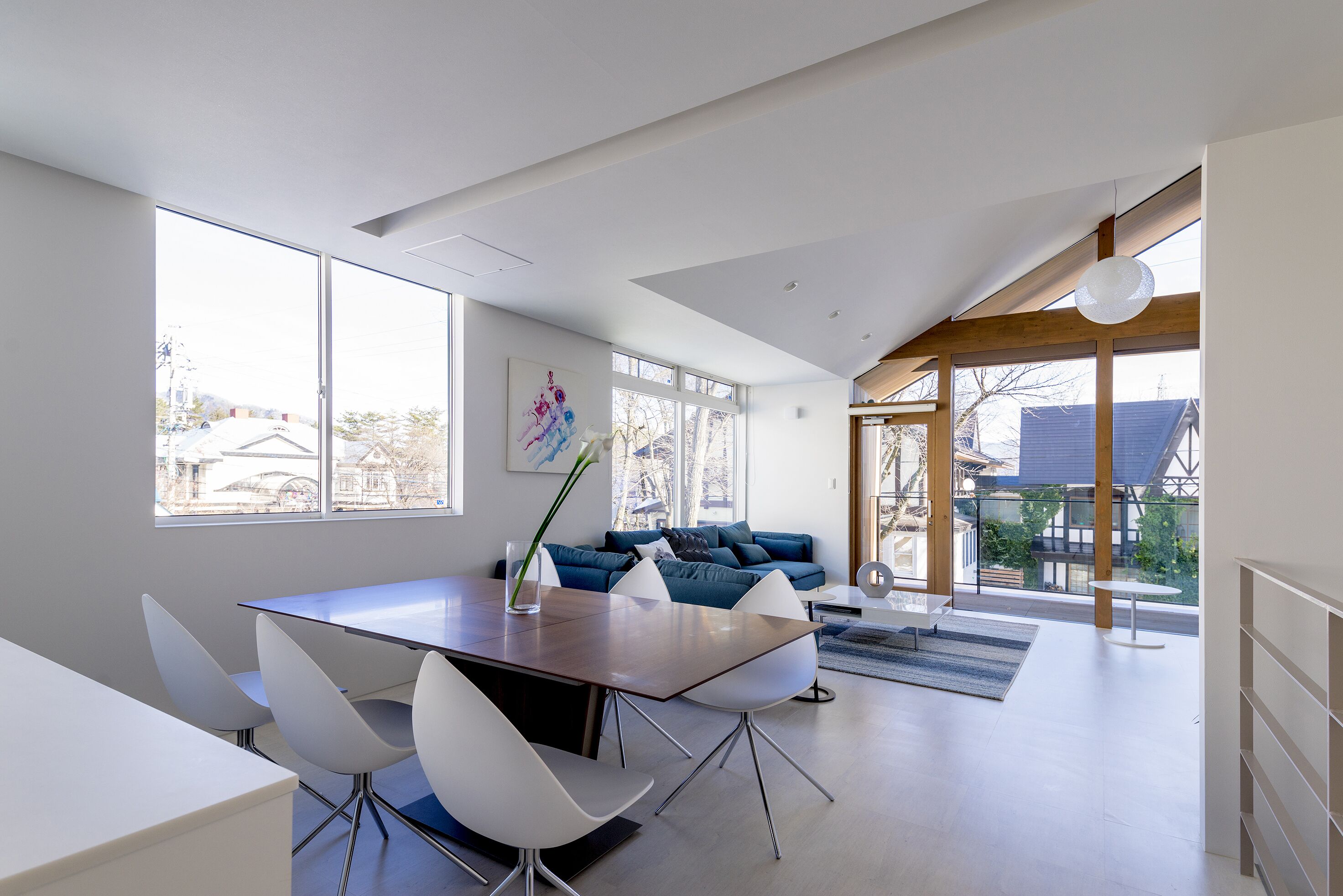 A modern living space with a dining area, a sofa set, and large windows providing natural light.