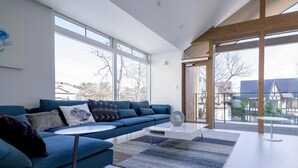 A modern living room with a blue sofa, a white coffee table, and large windows offering a view of the outside. - White Fox Chalet (Hakuba)