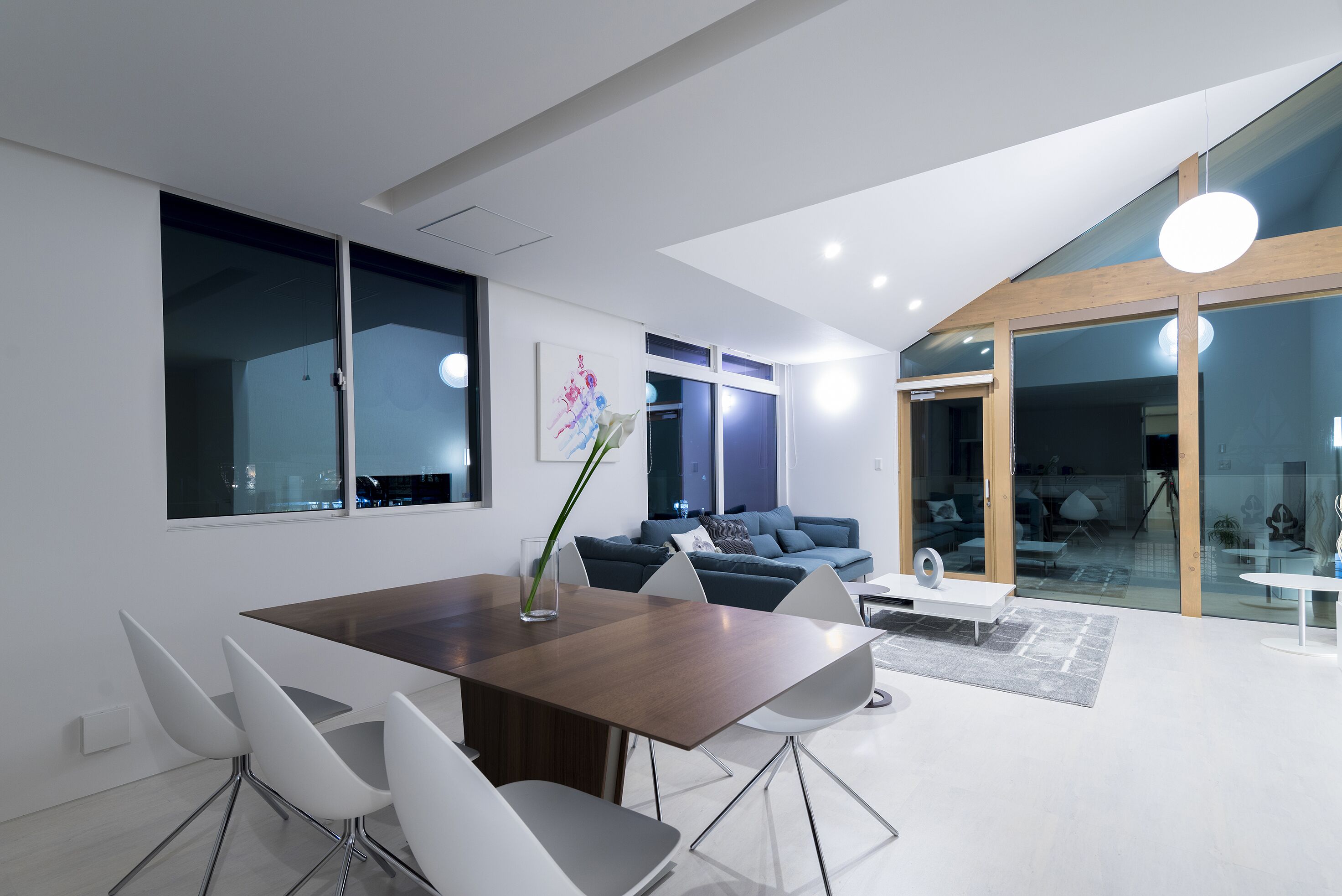 A modern living room with a dining area, featuring a large wooden table, white chairs, and a blue sofa.