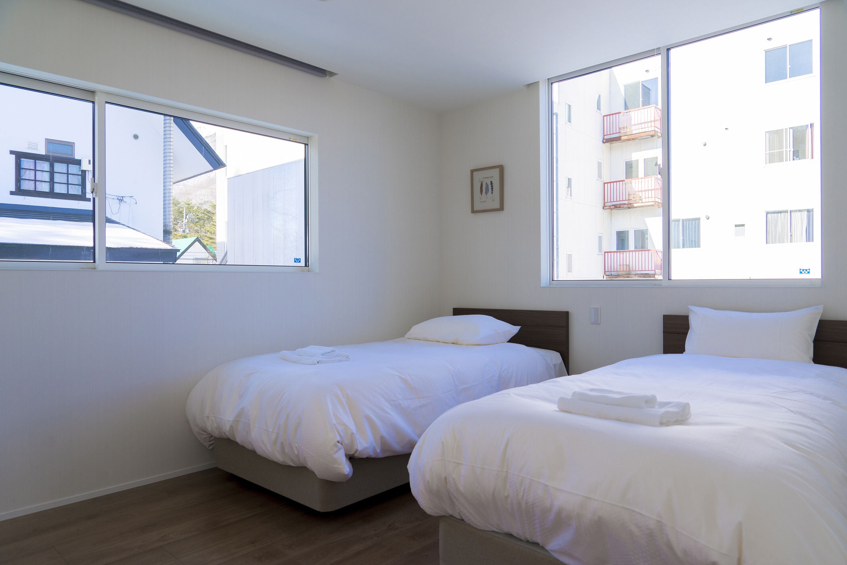 A bedroom with two beds, large windows, and a view of a building outside.