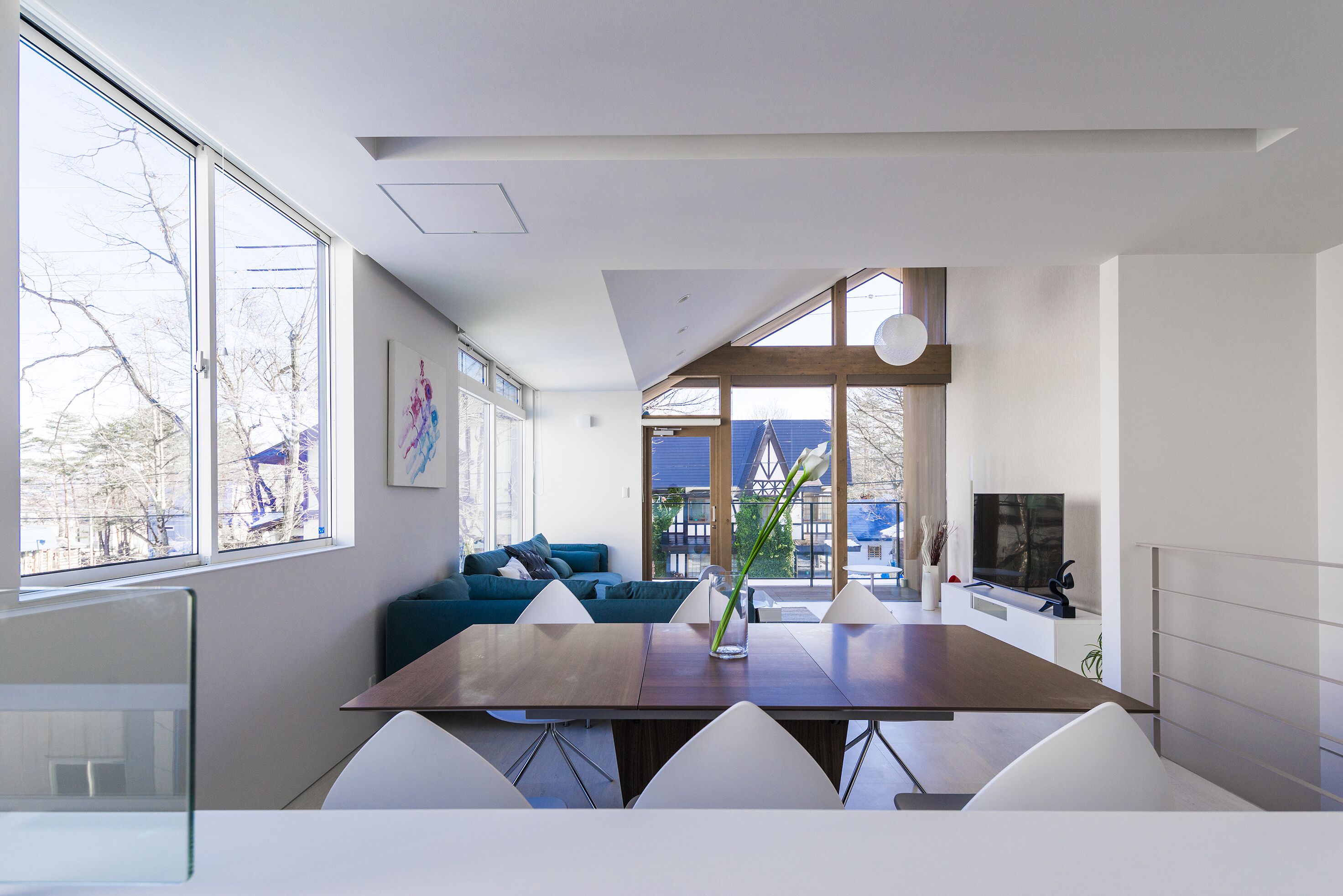 A modern living room with a dining area, large windows, and a view of the outside.