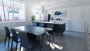A modern kitchen with a central island, a dining area with a table and chairs, and a large window providing natural light. - White Fox Chalet (Hakuba)